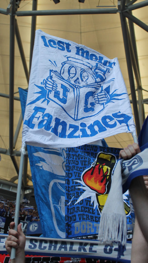 Fans halten Doppelhalter hoch mit der Aufschrift "Lest mehr Fanzines"