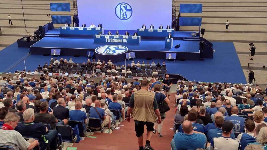 Mitgliederversmmlung 2023. Ein Mann geht die Treppe durch volle Ränge hinunten, im Hintergrund die Bühne für den Aufsichtsrat.