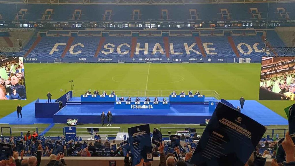 Fans halten auf der Mitgliederversammlung 2025 in der Arena Stimmkarten hoch. Im Hintergrund die Bühne mit Vorstand und Aufsichtsrat.